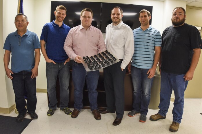 Dung Su, Frank Neukam, Sam Pratt, Jonathan Hopkins, Keith Brennan and Ryan Franke, all employees with Naval Surface Warfare Center, Carderock Division, display additively manufactured aviation part they rapidly produced in a first-of-its-kind response to a critical fleet need in West Bethesda, Md., May 31, 2017. Carderock engineers collaborated with other commands from the Additive Manufacturing Warfare Center Working Group, including NSWC Indian Head and Dahlgren and Combat Directions Systems Activity Dam Neck, to fulfill a request from Naval Air Systems Command for parts to restore stalled training operations for the T-45 Goshawk. (U.S. Navy photo by Dustin Q. Diaz/Released)