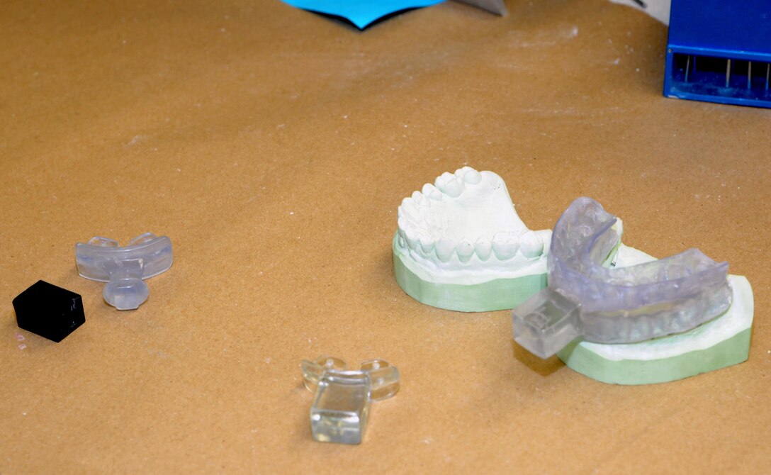 The completed dental appliance (right) fabricated by the 88th Dental Squadron Dental Lab incorporates the accelerometer holder (center) into one custom-made and easy-to-use unit for the ejection seat research performed by the 711th Human Performance Wing’s Applied Neuroscience Branch. The unitized device effectively replaces the carrier and holder (left) previously attached to a commercially-produced sports mouth guard which often failed during critical testing. (U.S. Air Force photo/Will Huntington)