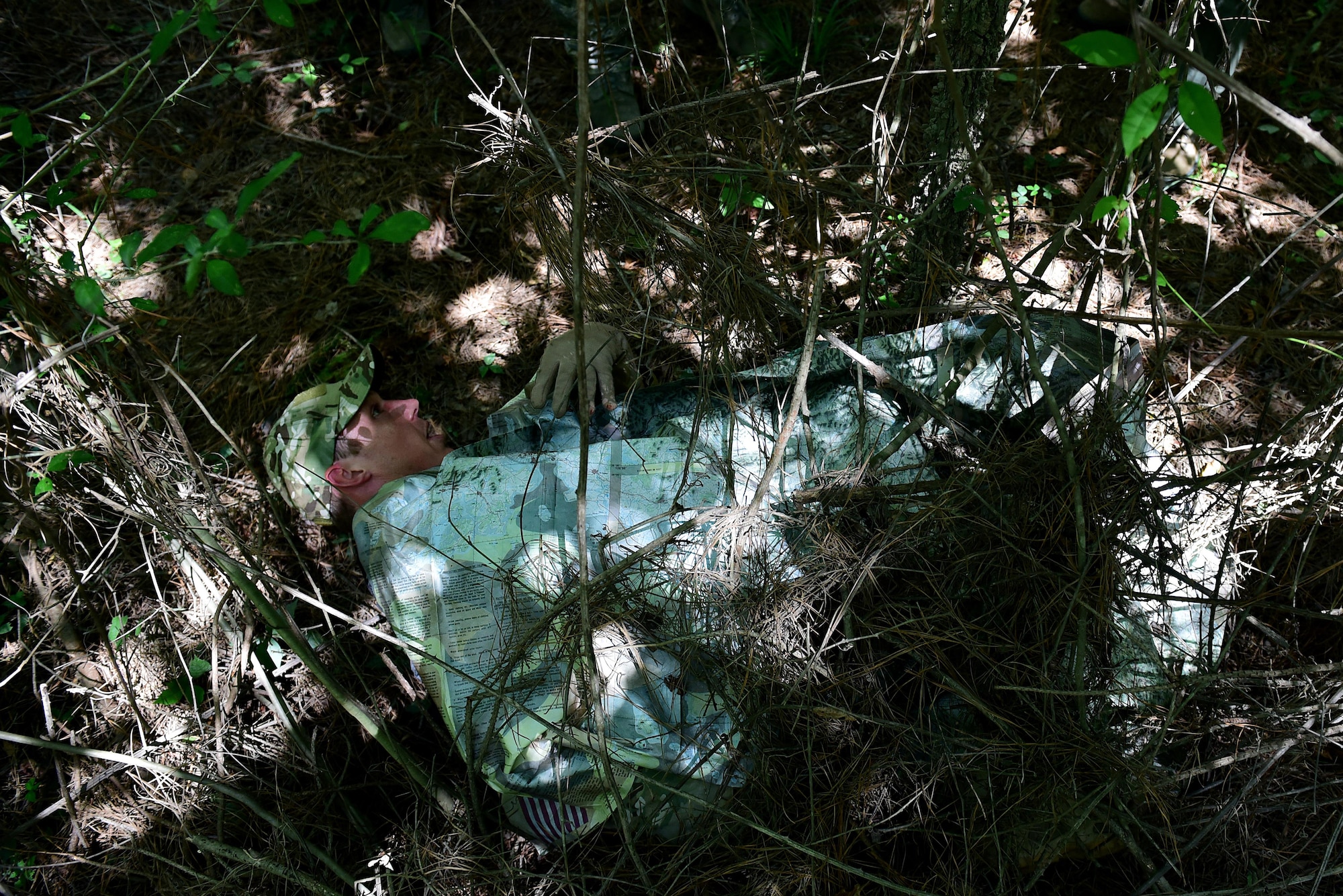Staff Sgt. Joshua Krape, 4th Operations Support Squadron survival, evasion, resistance and escape specialist, demonstrates how to quickly create a shelter using the environment and a map during a combat survival training course, June 27, 2017, at Howell Woods, Four Oaks, North Carolina. According to Krape, having a shelter that blends into the environment can keep downed aircrew alive when they are trapped behind enemy lines. (U.S. Air Force photo by Airman 1st Class Kenneth Boyton)