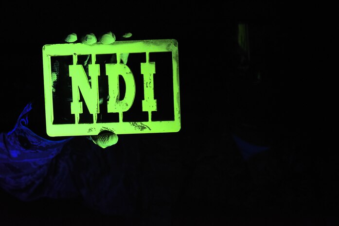 Senior Airman Brett Gyurnek, 437th Maintenance Squadron Non-Destructive Inspection technician, holds up a piece of inscribed metal covered in fluorescent penetrant under an ultraviolet light at Joint Base Charleston, S.C. July 11, 2017. The Airmen of the 437th MXS NDI shop use diagnostic procedures to determine if aircraft parts are unsafe or compromised.