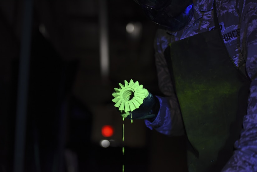 Senior Airman Brett Gyurnek, 437th Maintenance Squadron Non-Destructive Inspection technician, retrieves a core reverser gear from a vat of fluorescent penetrant during a deficiency inspection at Joint Base Charleston, S.C. July 10, 2017. Fluorescent penetrant testing is a reliable way to illuminate fractures on the surface of damaged aircraft parts. It is done by submerging the part in a fluorescent liquid and allowing the dye to penetrate into any cracks. The liquid is then rinsed off and placed in a developing agent which makes the fluorescent liquid illuminate brighter under an ultraviolet light. The part is then placed under an ultraviolet light and, if cracks are present, they will light up making the deficiency more visible.