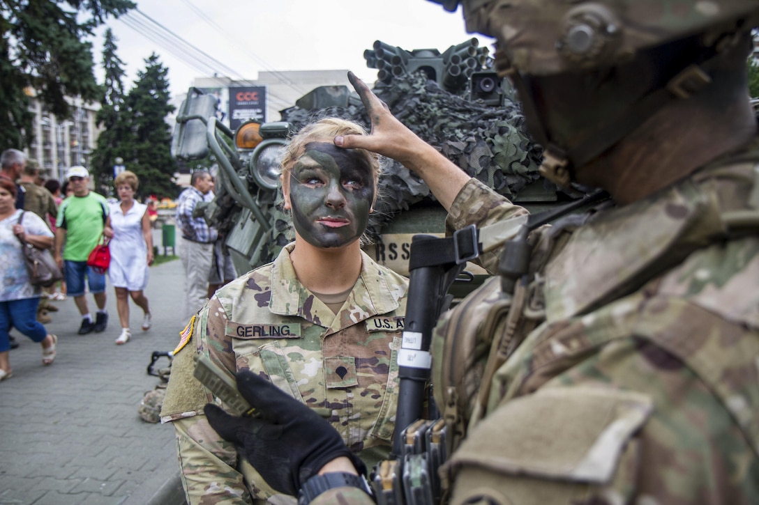 A soldier applies camouflage paint to another soldier as their unit hosts a static display of stryker vehicles during Dragoon Guardian, an exercise in Ploiești, Romania, July 12, 2017. Army photo by Capt. Jeku Arce