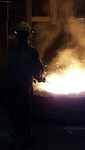 A Buck Company employee stirring molten metal to pull out impurities.