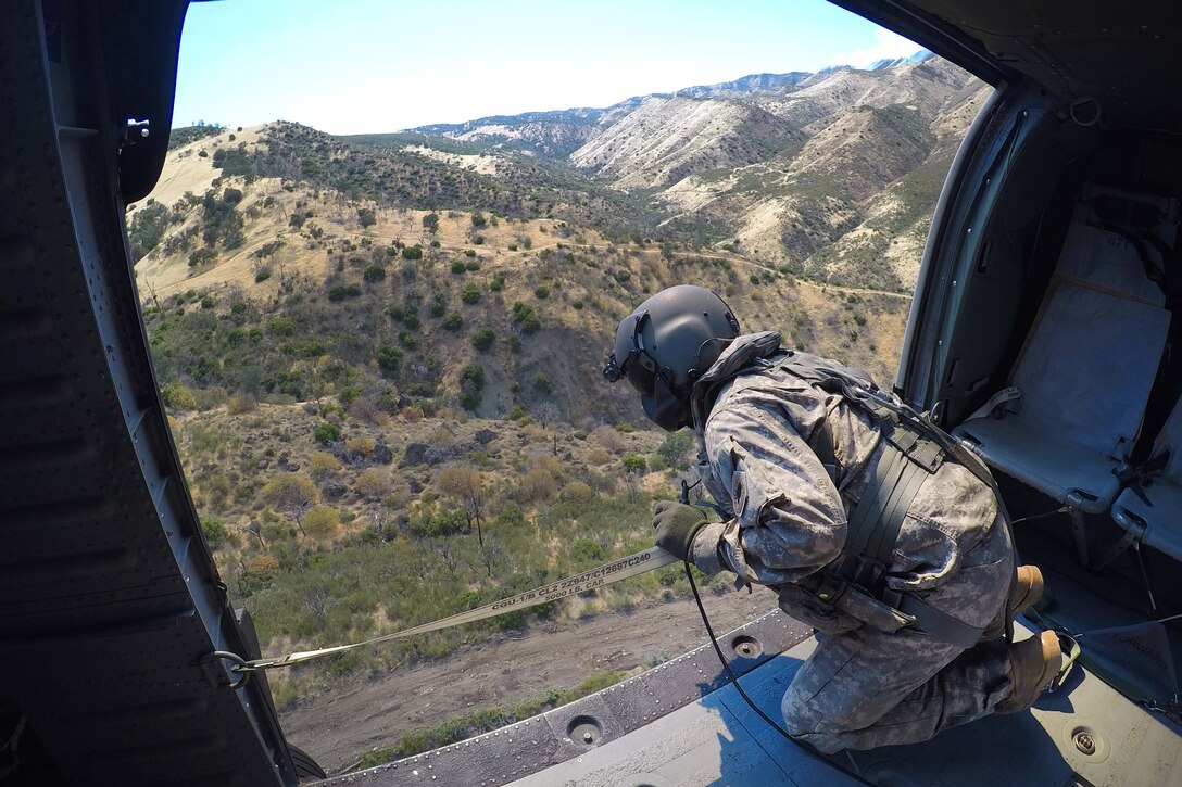 California Army National Guard Staff Sgt. Ge Xiong watches while a 2,600-gallon bucket firefighting system drops water from a UH-60 Black Hawk helicopter on the Garza Fire in Kings County, California, July 13, 2017. Xiong is a crew chief assigned to the California Army National Guard’s 1106th Theater Aviation Sustainment Maintenance Group. Army National Guard photo by Staff Sgt. Eddie Siguenza