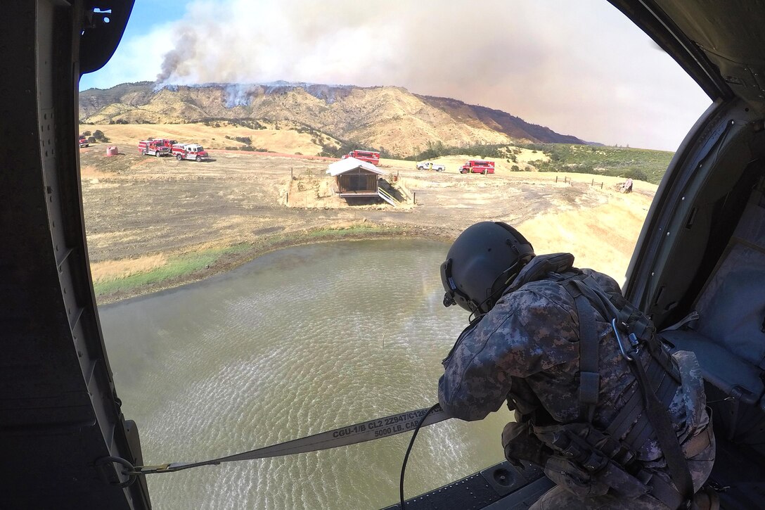 California Army National Guard Staff Sgt. Ge Xiong watches from a UH-60 Black Hawk helicopter as a 2,600-gallon bucket firefighting system is refilled with water during efforts to fight the Garza Fire in Kings County, California, July 13, 2017. Xiong is a crew chief assigned to the California Army National Guard’s 1106th Theater Aviation Sustainment Maintenance Group. Army National Guard photo by Staff Sgt. Eddie Siguenza