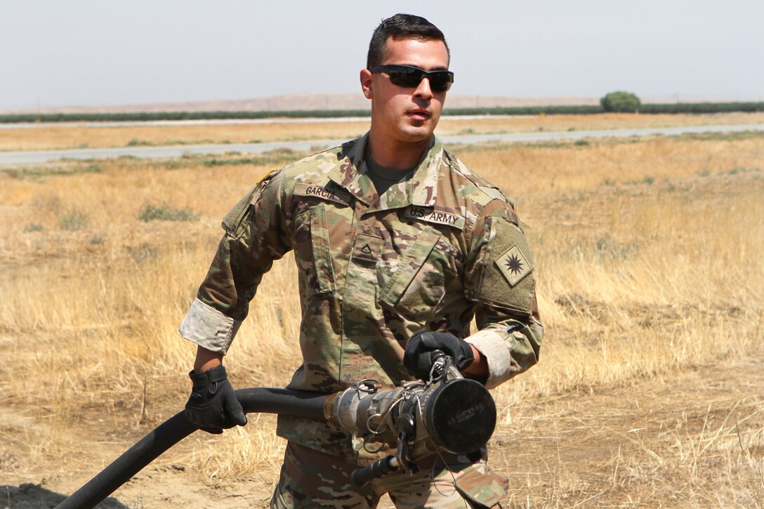 California Army National Guard Pfc. Vicente Garcia stretches a fuel pump to a UH-60 Black Hawk helicopter for refueling at Coalinga Municipal Airport, Fresno County, California, July 13, 2017, before continuing firefighting efforts during the Garza Fire in Kings County. Garcia is assigned to the California Army National Guard’s Company E, 1st Battalion, 140th Aviation Regiment. Army National Guard photo by Staff Sgt. Eddie Siguenza