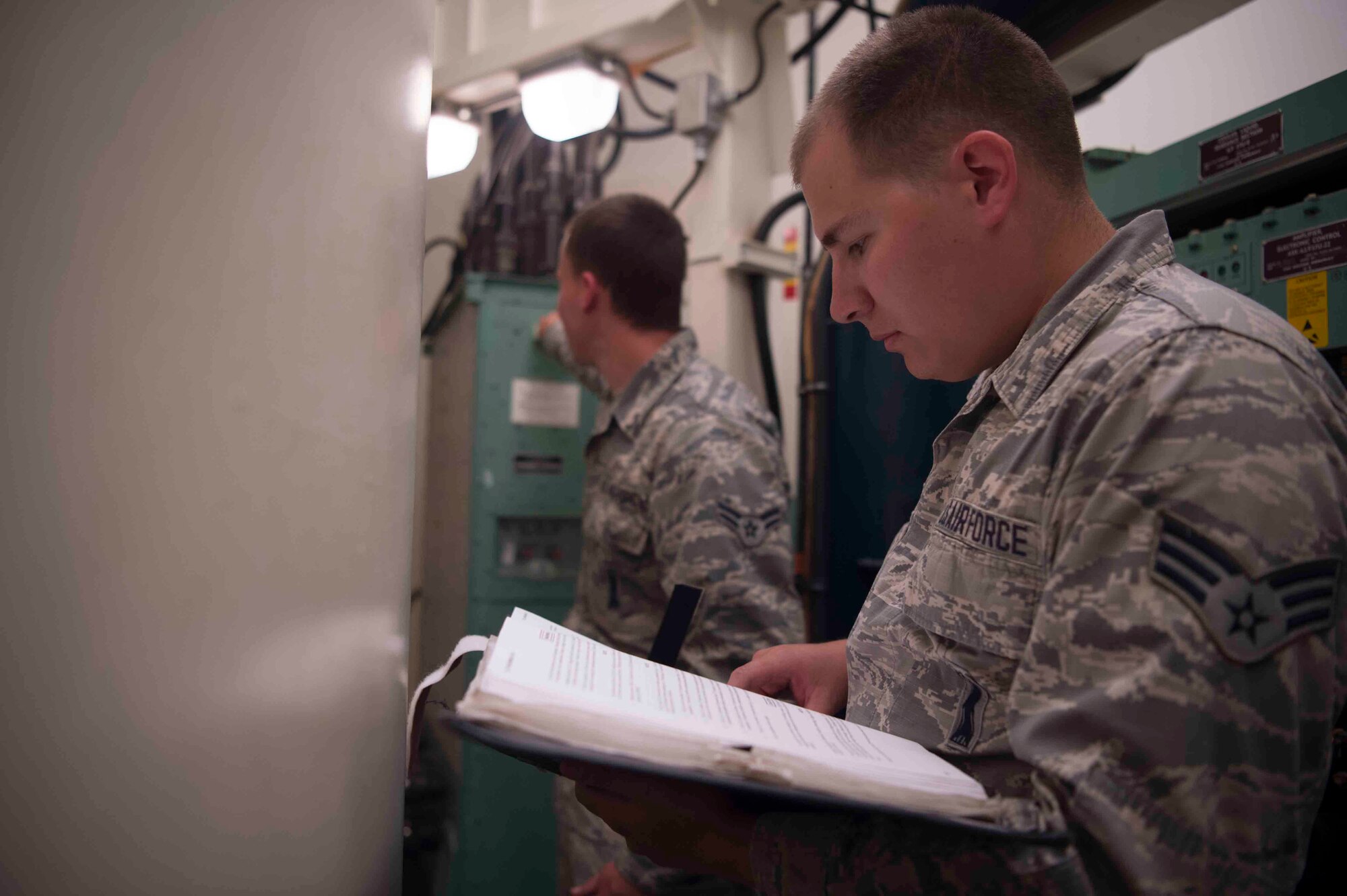 Senior Airman Major Santiago, 90th Missile Maintenance Squadron team chief, reads through the technical order while Airman 1st Class Alex Medellin, 90th MMXS team member, sets up the safety control switch key inside the launch facility during code change in the 90th Missile Wing missile complex, June 20, 2017. The SCS key disables the missile from launching to allow the maintainers to work at the site safely. Code change ensures the safety, security and effectiveness of America’s ICBM arsenal, which is the bedrock of nuclear deterrence. (U.S. Air Force photo by Staff Sgt. Christopher Ruano)