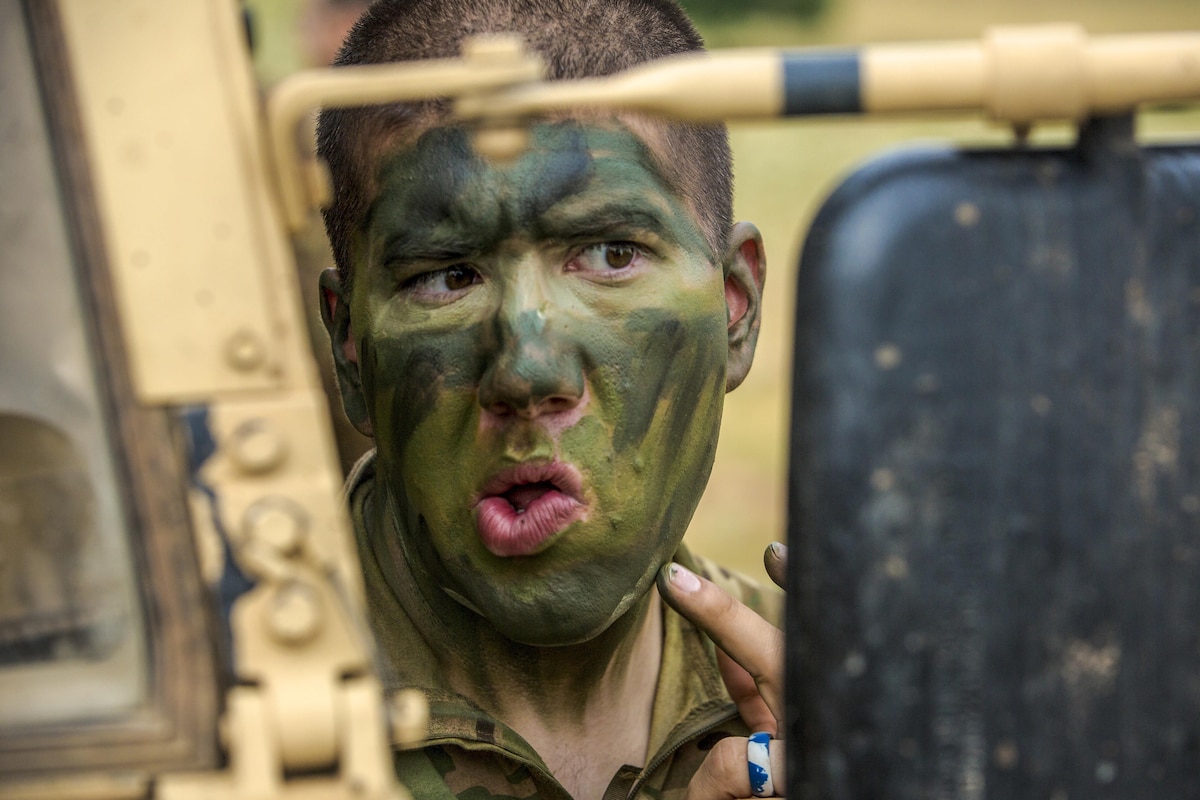 A soldier applies face paint using a vehicle's mirror.