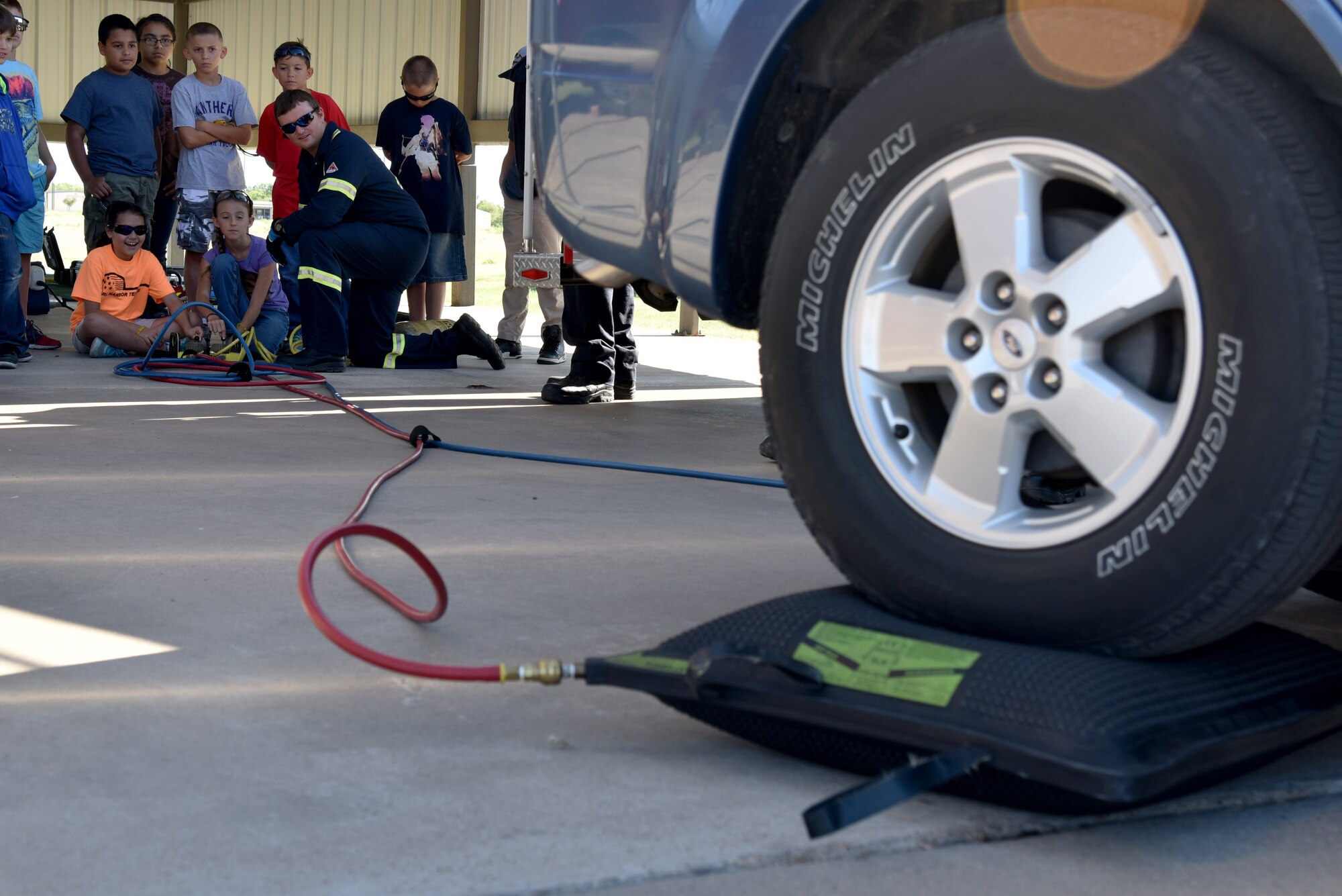 Jay Teague, 17th Civil Engineer Squadron firefighter, teaches Addalynn Krickland and Josilyn Teague, junior firefighters, how to use compressed air to lift a vehicle during the junior firefighter camp at the fire station on Goodfellow Air Force Base, Texas, July 11, 2017. During the weeklong course, the children learned how to use fire extinguishers, tie a variety of knots and how to safely climb and descend a ladder. (U.S. Air Force photo by Staff Sgt. Joshua Edwards/Released)