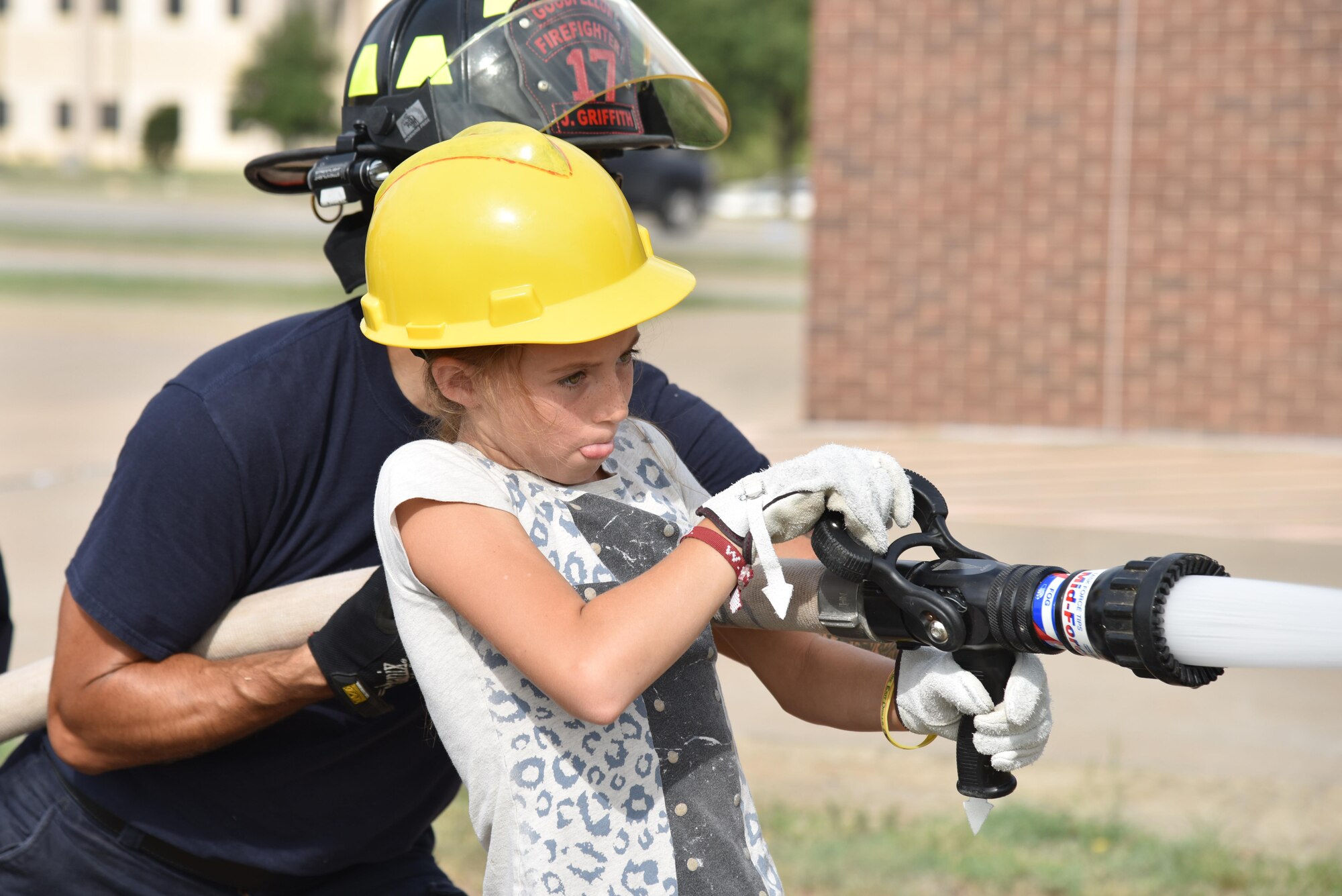 Josilyn Teague, junior firefighter, sprays a fire hose during the junior firefighter camp at the fire station on Goodfellow Air Force Base, Texas, July 13, 2017. Teague practiced shooting a basketball to test her aim. (U.S. Air Force photo by Staff Sgt. Joshua Edwards/Released)