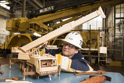 Jeff Iller, a Code 722 crane inspector, shows off a wood crane he made of walnut and maple that resembles a GMK mobile hydraulic extendable boom crane. The two-foot long crane has a boom which extends to 52 inches. 
