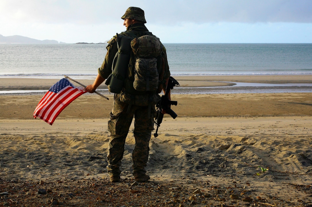 Army Spc. Shawn Spafford stands on a beach with an American flag during exercise Talisman Saber at Shoalwater Bay, Queensland, Australia, July 14, 2017. Army National Guard photo by Sgt. Alexander Rector