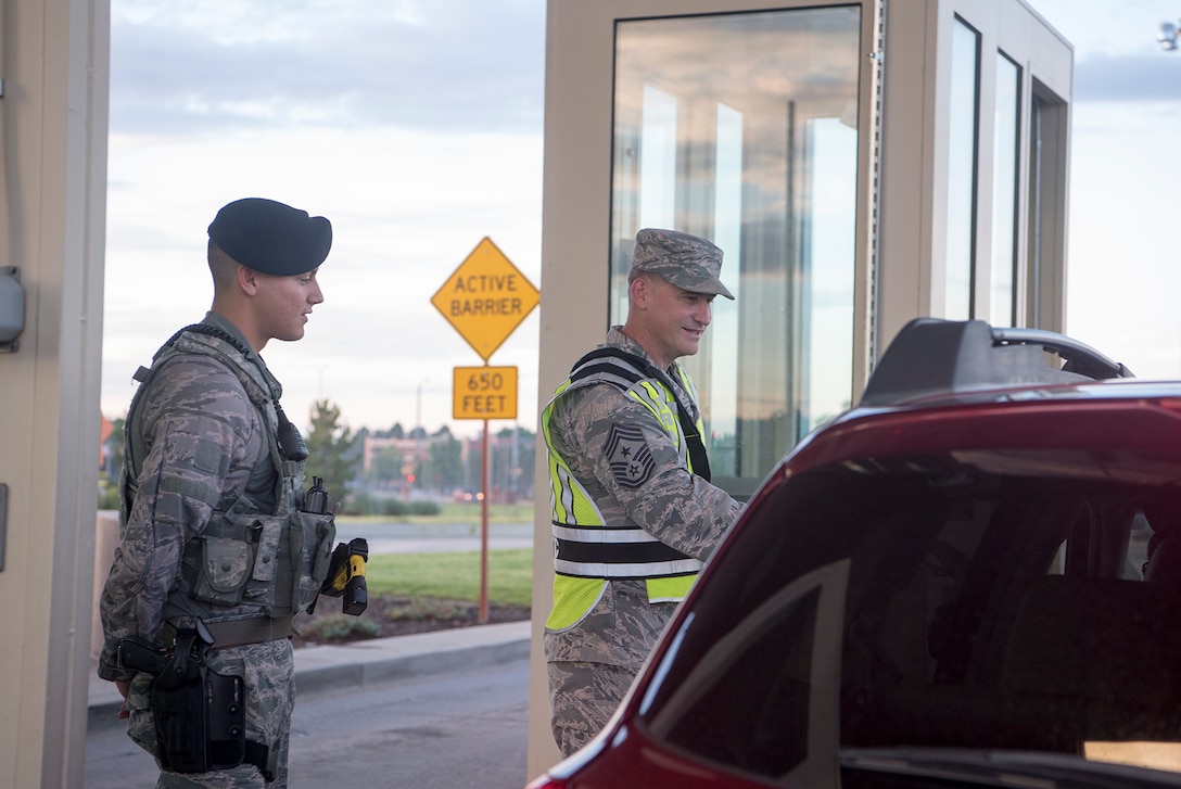 PETERSON AIR FORCE BASE, Colo. – Chief Master Sgt. Mark Bronson, 21st Space Wing command chief, checks ID cards alongside Airmen 1st Class Andrew Brem, 21st Security Forces Squadron installation entry controller, at the West gate of Peterson Air Force Base, Colo., July 13, 2017. Bronson was at the gate during Chiefs Development Week, a week designed to allow chief master sergeants to offer face to face mentorship to Airmen of all ranks. (U.S. Air Force photo by Steve Kotecki)
