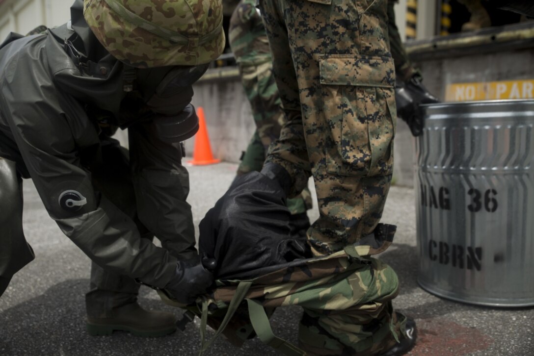A Japanese Ground Self-Defense service member helps U.S. Marine Lance Cpl. Enrique Puentes Jr. get out of his Mission Oriented Protective Posture suit during a simulated joint study at Marine Corps Air Station Futenma, Okinawa, Japan, July 13, 2017. The JGSDF service member is with 15th Nuclear, Biological, Chemical Defense Unit. Puentes, a native of Tampa, Florida, is a CBRN defense specialist with Marine Wing Headquarters Squadron 1. (U.S. Marine Corps photo by Cpl. Kelsey Dornfeld). 