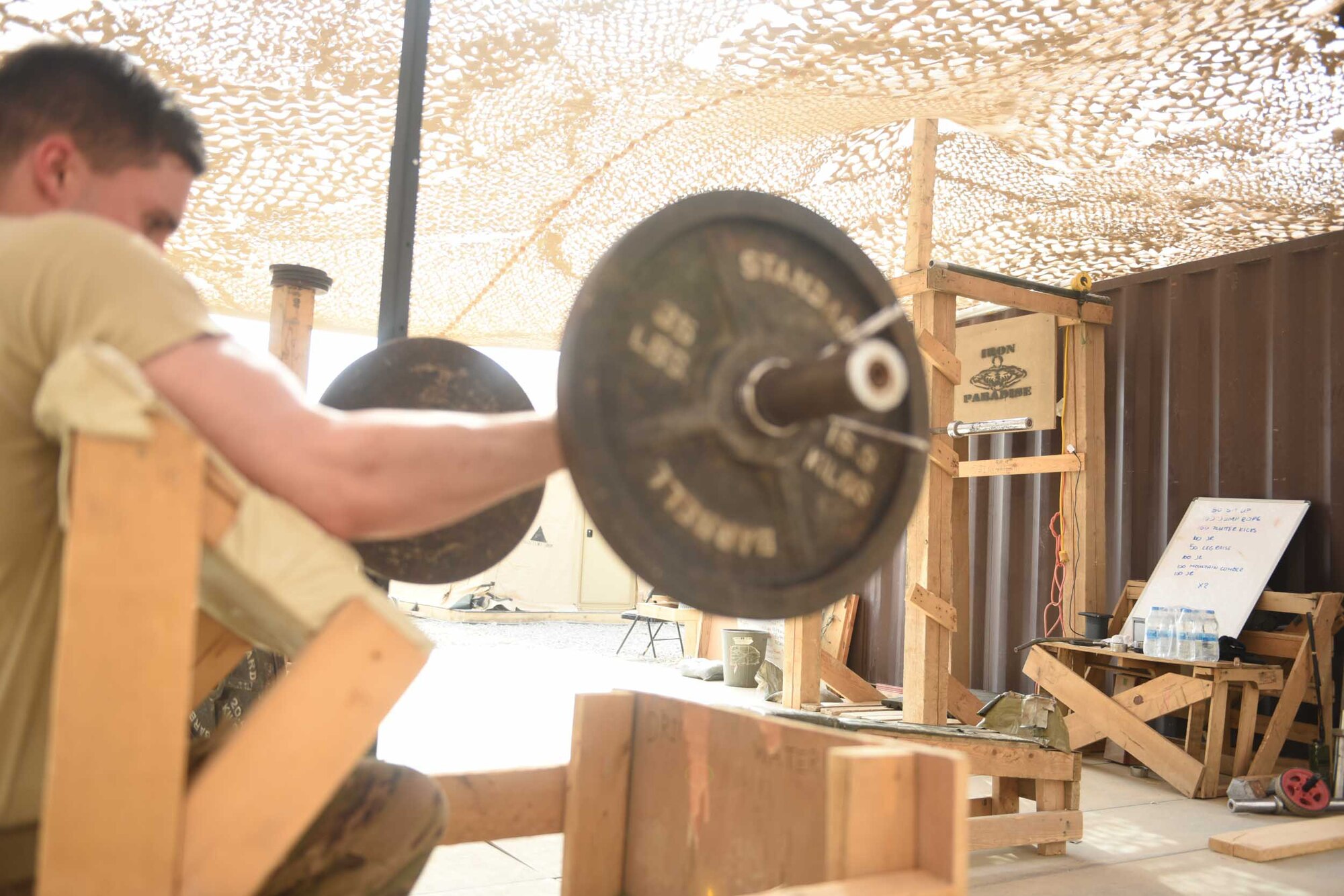 U.S. Air Force Senior Airman Justin Salisbery, an airfield management specialist deployed in support of Combined Joint Task Force – Operation Inherent Resolve and assigned to the 370th Air Expeditionary Advisory Group, Detachment 1, curls a barbell on a makeshift preacher curl bench in the 370th AEAG detachment’s “Iron Paradise” gym at Qayyarah West Airfield, Iraq, July 2, 2017. The air advisors built the “Iron Paradise” gym, which includes a makeshift squat rack, bench press, preacher curl bench and other recently acquired weights, creating an area often filled with U.S. Air Force and Army personnel trying to maintain physical fitness in their austere location. CJTF-OIR is the global Coalition to defeat ISIS in Iraq and Syria.   (U.S. Air Force photo by Tech. Sgt. Jonathan Hehnly)