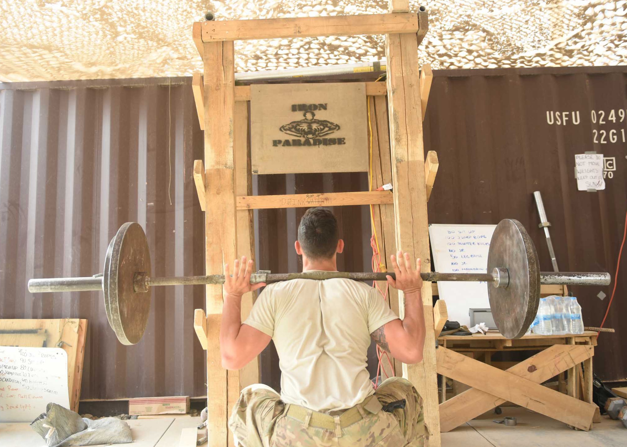 U.S. Air Force Airman 1st Class Zachary Tilley, an expeditionary maintenance liaison specialist deployed in support of Combined Joint Task Force – Operation Inherent Resolve and assigned to the 370th Air Expeditionary Advisory Group, Detachment 1, performs a barbell squat in front of a makeshift squat rack in the 370th AEAG detachment’s “Iron Paradise” gym at Qayyarah West Airfield, Iraq, July 2, 2017. The air advisors built the “Iron Paradise” gym, which includes a makeshift squat rack, bench press, preacher curl bench and other recently acquired weights, creating an area often filled with Air Force and Army personnel trying to maintain physical fitness in their austere location. CJTF-OIR is the global Coalition to defeat ISIS in Iraq and Syria. (U.S. Air Force photo by Tech. Sgt. Jonathan Hehnly)
