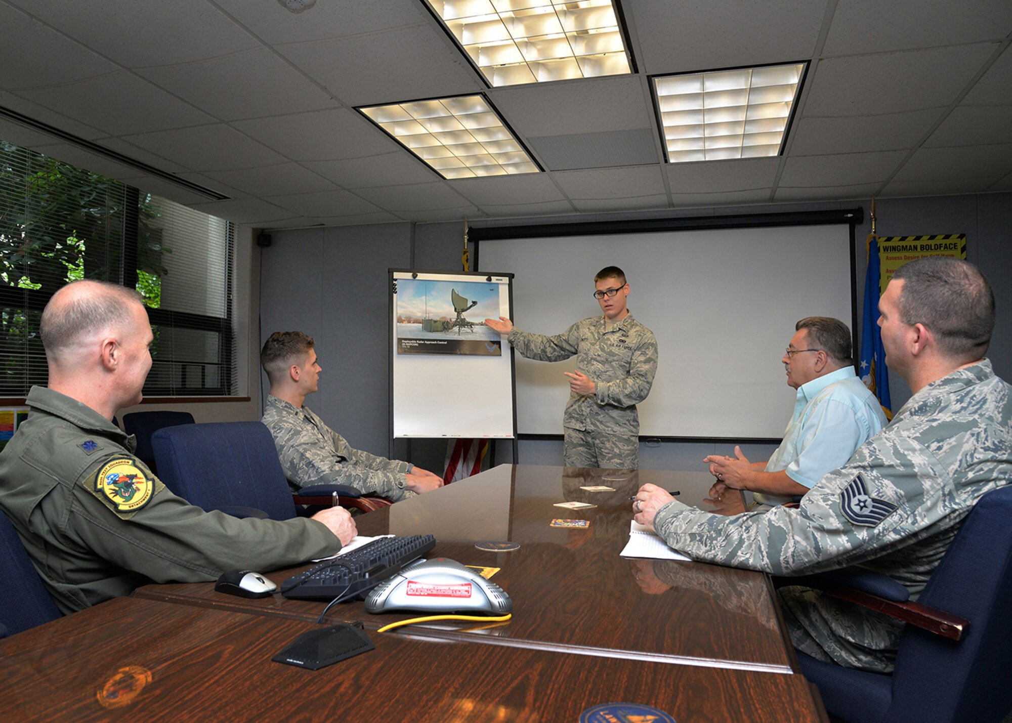 Second Lt. Nic Cincotti, Command and Control test manager, 46th Test Squadron, Detachment 1, speaks to other members of the detachment about the support the group provides to program offices at Hanscom Air Force Base, Mass., July 13. Listening at the table from left-to-right is Lt. Col. Corey Beaverson, commander; 1st Lt. Matt Neau, C2 Cybersecurity test engineer; Jim Bordini, test engineer; and Tech. Sgt. James Pryor, Cybersecurity test manager. The detachment supports Hanscom by being the access point to the test community. (U.S. Air Force photo by Linda LaBonte Britt)