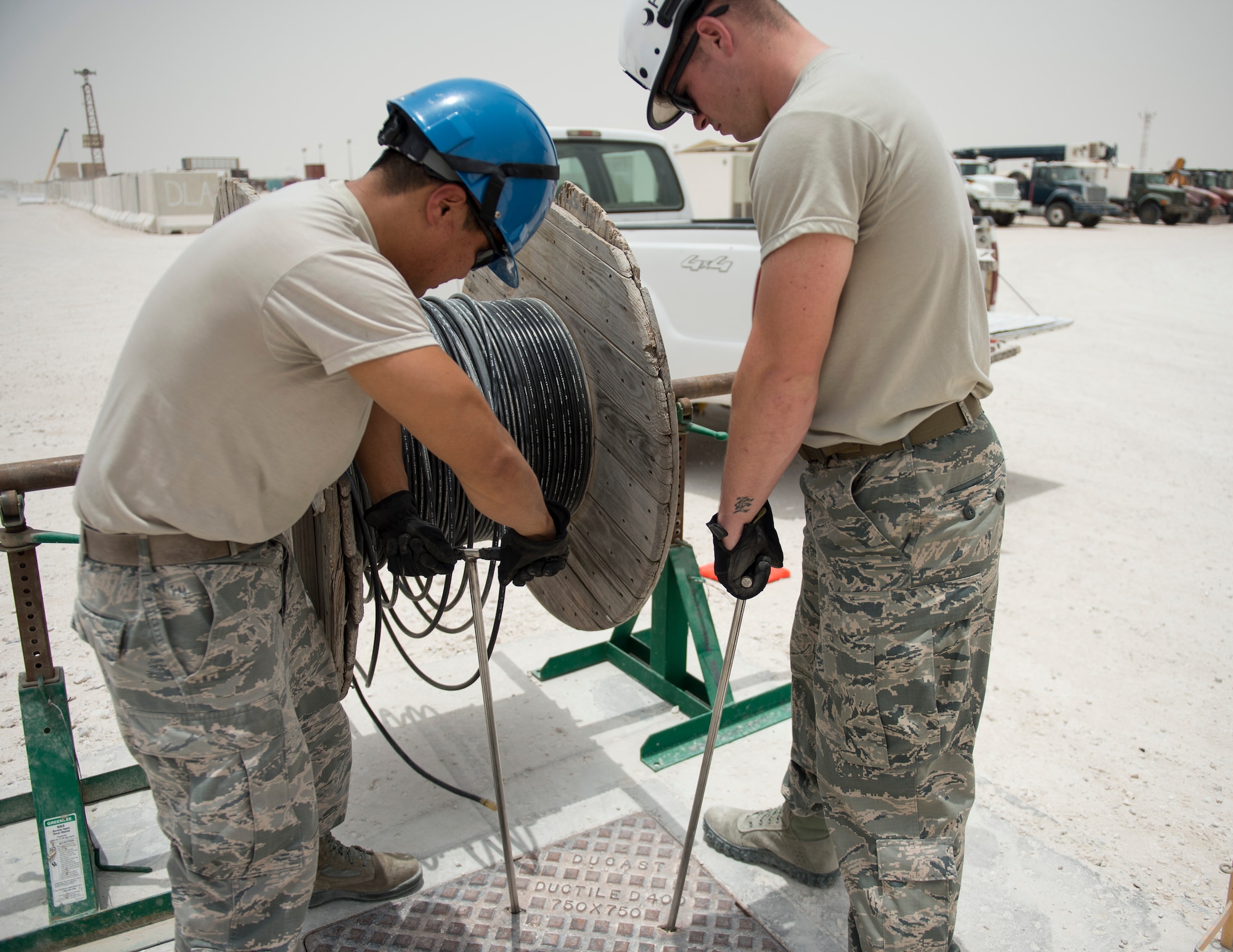 U.S. Air Force Senior Airmen Robert Yurko, right, and Ebby Bryce, cable and antenna system specialists with the 379th Expeditionary Communication Squadron, prepares to remove a communication manhole cover at Al Udeid Air Base, Qatar, July 14, 2017.  Yurko and Bryce are part of a team of airmen that are responsible for installing, sustaining, and repairing miles of copper and fiber optics cables at Al Udeid Air Base. (U.S. Air Force photo by Tech. Sgt. Amy M. Lovgren)