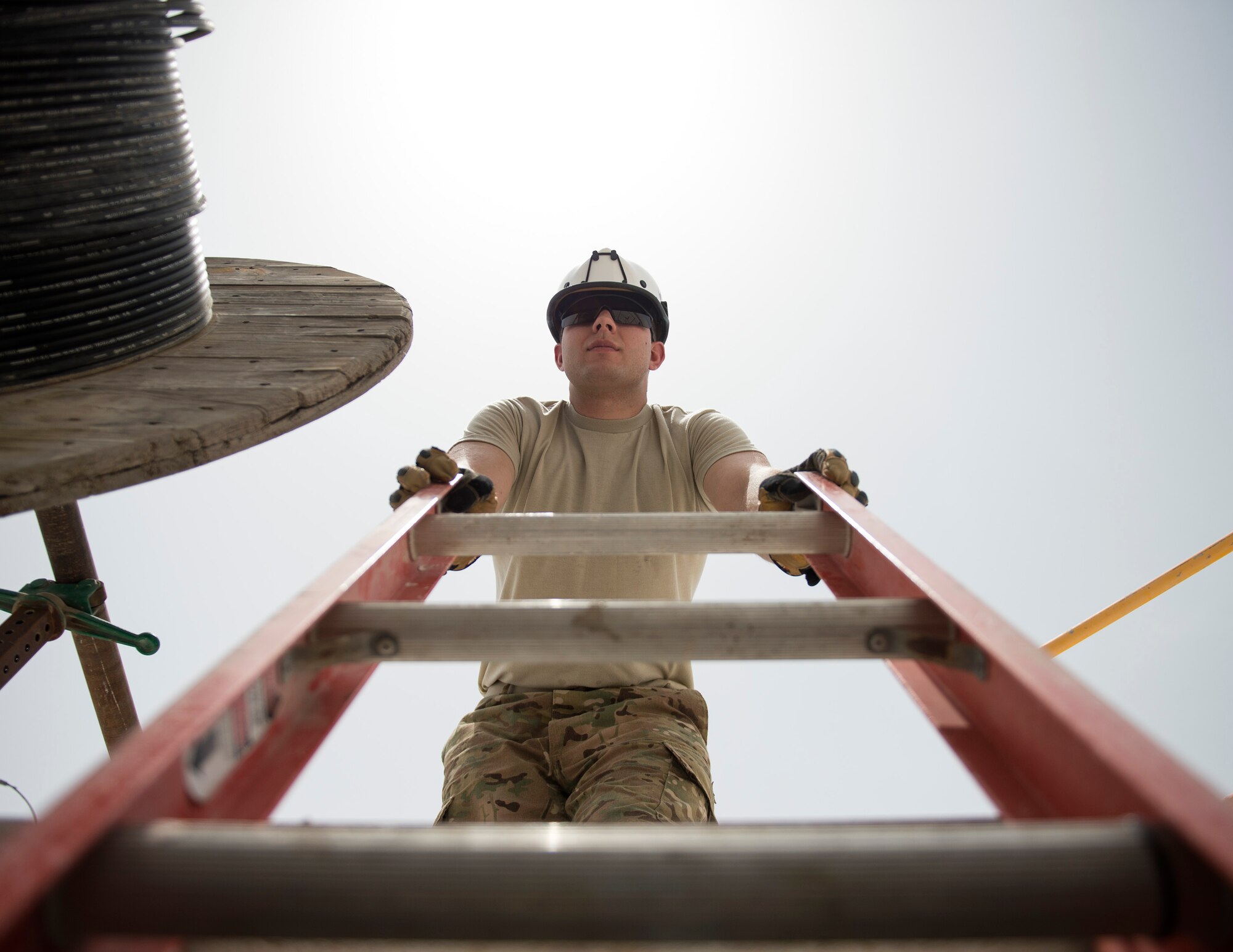 U.S. Air Force Senior Airman Ebby Bryce, a cable and antenna system specialist with the 379th Expeditionary Communication Squadron, holds the ladder at Al Udeid Air Base, Qatar, July 14, 2017. Bryce is part of team of airmen that is responsible for installing, sustaining, and repairing miles of copper and fiber optics cables at Al Udeid Air Base. (U.S. Air Force photo by Tech. Sgt. Amy M. Lovgren)