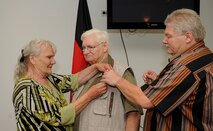 Thomas Perry (middle), retired from the 786th Force Support Squadron after 48 years of service, receives an award presented by his wife and son at the Lindberg Hof Dining Facility, Kapaun Air Station, June 30, 2017. Retiring at the top of his game, Mr. Perry was the Lindberg Hof Dining Facility’s top chef the last nice years before his retirement. (U.S. Air Force photo by Airman 1st Class Savannah L. Waters)