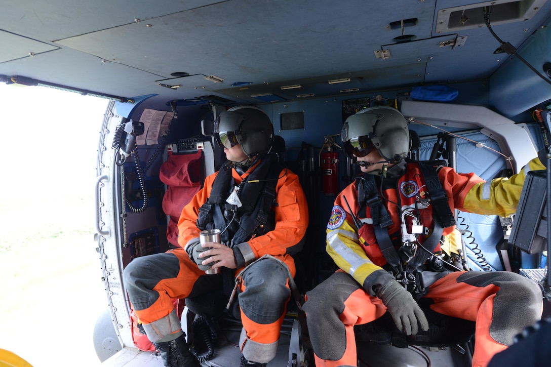 Coast Guard Petty Officers 2nd Class Adam Campbell, left, and Andrew Stover, aircrewmen on an MH-60 Jayhawk helicopter, watch as their helicopter departs on a training mission from Forward Operating Location Kotzebue in support of Operation Arctic Shield in Kotzebue, Alaska, July 16, 2017. Coast Guard photo by Lt. Brian Dykens.