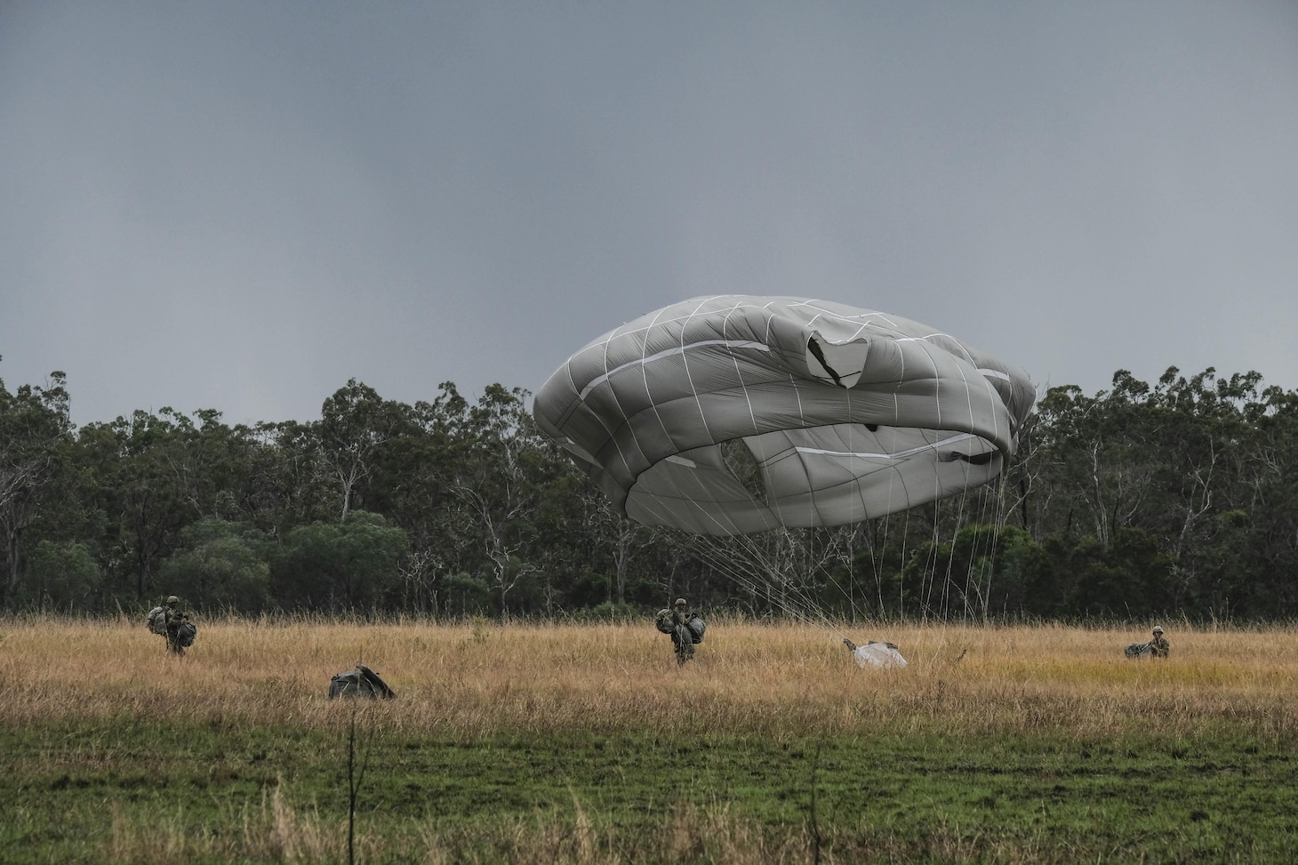 Paratroopers of 4th Infantry Brigade Combat Team (Airborne) 25th Infantry Division, move to a parachute collection zone while another lands in Shoalwater Bay, Queensland, Australia, July 13. The airborne operation was conducted as part of Exercise Talisman Sabre 2017, a massive, biennial exercise designed to exercise the partnership of joint forces throughout the Pacific region. (U.S. Army photo by Staff Sgt. Daniel Love)