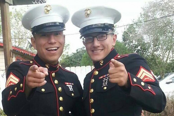 Two Marines standing next to each other smile and point at the camera.