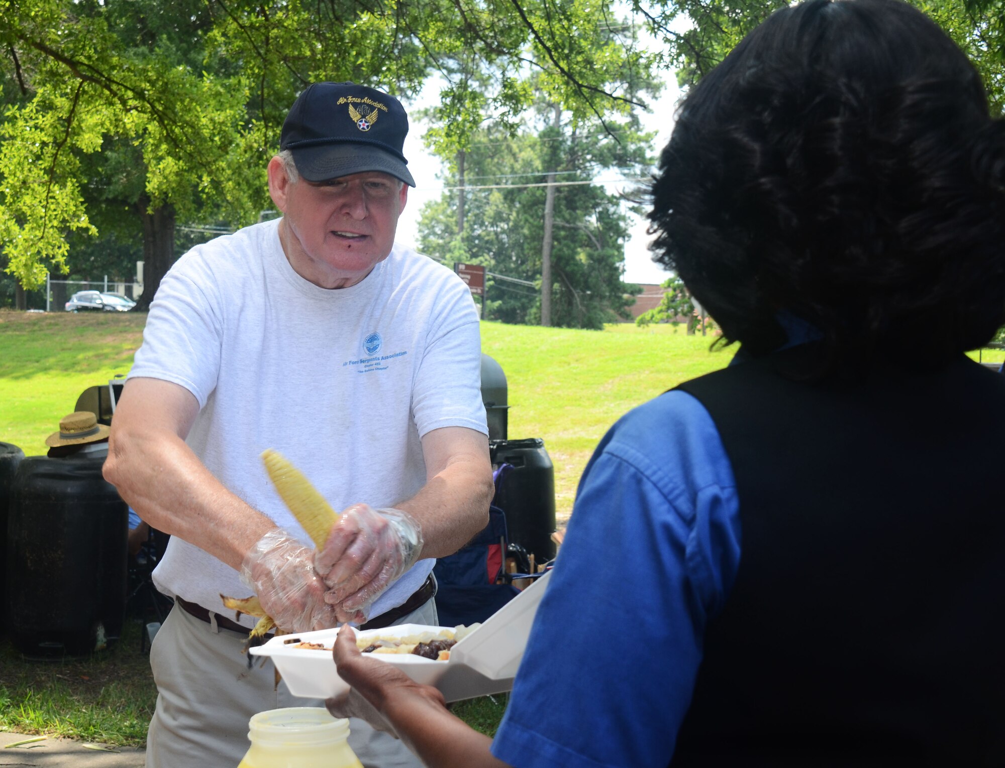 Retired Chief Master Sgt. David Curtis, serves ears of corn to an attendee at the annual Corn and Sausage Roast held on Dobbins Air Reserve Base, Ga. July 19, 2017. The event's proceeds, along with assistance from the Dobbins Thrift Store, benefit the Dobbins Emergency Relief Fund. (U.S. Air Force photo/Don Peek)