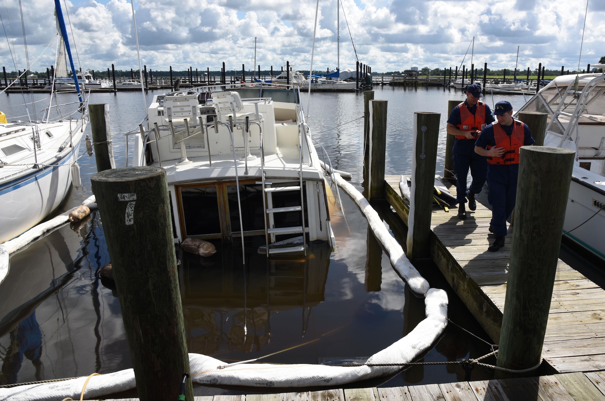 Petty Officer 2nd Class Clayton Taylor, Coast Guard Mobile Sector Incident Management Division marine science technician, Mobile, Al., and Petty Officer 2nd Class Ellery Landry, Coast Guard Mobile Sector Incident Management Division operations specialist, Mobile, Al., inspect a privately-owned boat that sunk in the marina July 19, 2017, on Keesler Air Force Base, Miss. Keesler and local agencies gathered to ensure appropriate guidelines and safety procedures were followed prior to retrieving the boat. (U.S. Air Force photo by Kemberly Groue)