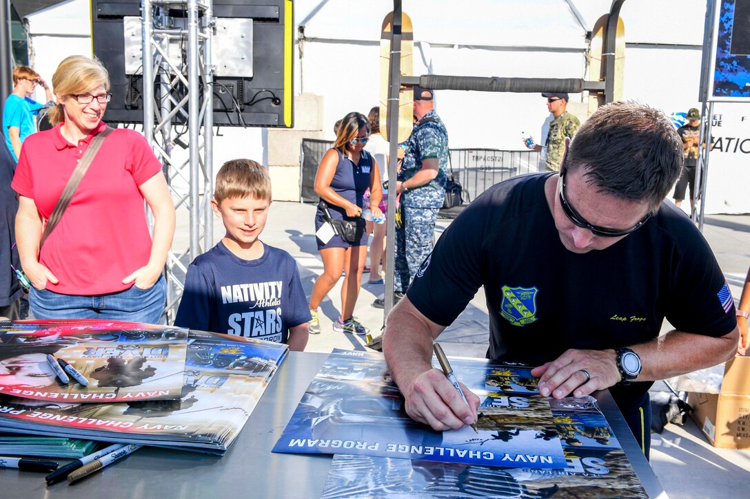 A member of U.S. Navy Parachute Team, “The Leap Frogs,” autographs a poster for a young fan after a skydiving demonstration in Elliot Park during a skydiving demonstration at the Summer X Games in Minneapolis, July 14, 2017. Navy photo by Petty Officer 3rd Class Kelsey L. Adams