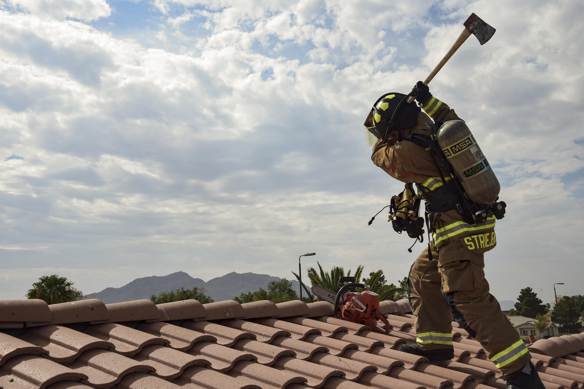 Airman 1st Class Adam Striejewske, 99th Civil Engineer Squadron firefighter, simulates breaking roof tiles during Red Flag 17-3 at Nellis Air Force Base, Nev., July 18, 2017. Breaking and removing roof tiles allows smoke from a building fire to escape easier. As the smoke leaves the building, rescue teams inside have better visibility to thoroughly search the building. (U.S. Air Force photo by Airman 1st Class Andrew D. Sarver/Released)