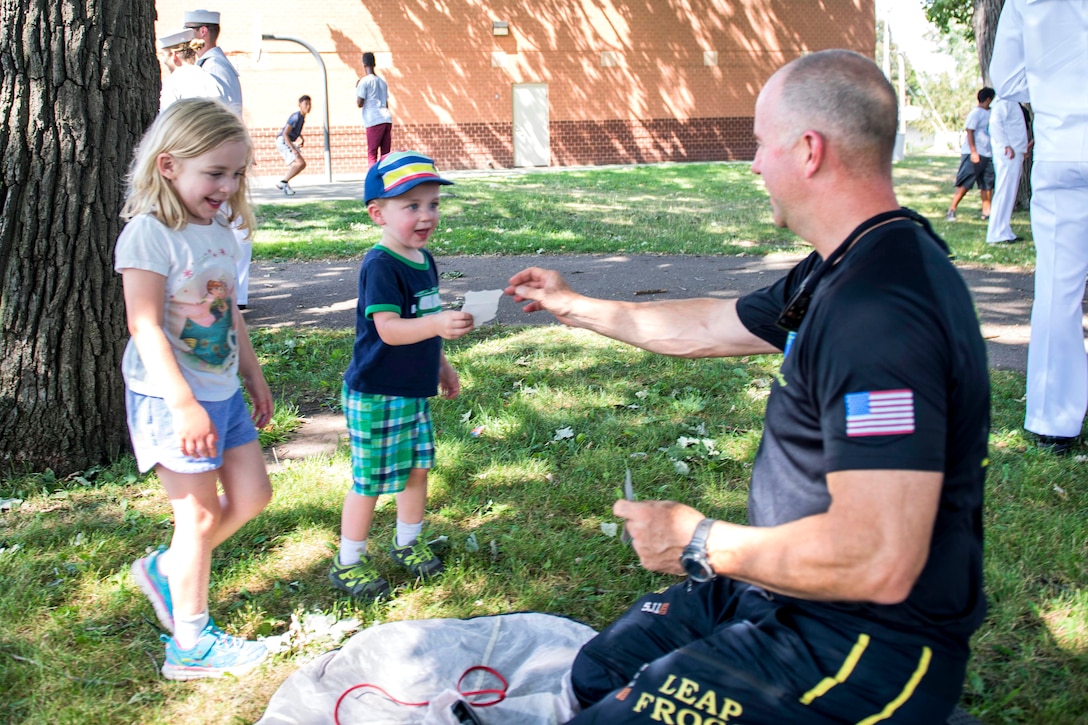 Retired Navy SEAL Jim Woods, a member of U.S. Navy Parachute Team “The Leap Frogs,” gives stickers to young fan after a skydiving demonstration at Hazel Park during Minneapolis/St. Paul Navy Week in Minneapolis, July 17, 2017. Navy photo by Petty Officer 3rd Class Kelsey L. Adams