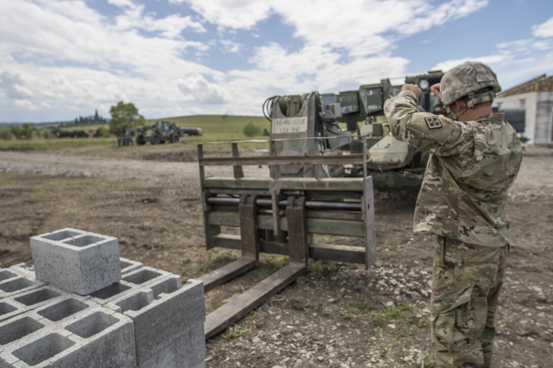 U.S. Army Reserve Soldier, Sgt. Byron Haynes, 733rd Engineer Company, Greenville, S.C. guides a U.S. Army Reserve Soldier, with  hand signals, to move a pallet of cinder blocks during Resolute Castle 17 at Cincu, Romania, July 15, 2017. Haynes, who is a highway inspector, in South Carolina, traveled to Romania with his company to help complete construction of a new training facility that will provide Allied forces the opportunity to prepare for potential conflict. The entire operation is led by U.S. Army Reserve engineers, who moved Soldiers and equipment from the U.S. to Romania over a period of several weeks to complete the training facility. Resolute Castle improves interoperability, enhances confidence and security assurance between partner nations, while improving infrastructure, capability and capacity at select locations throughout Europe. (U.S. Army Reserve photo by Staff Sgt. Felix R. Fimbres)