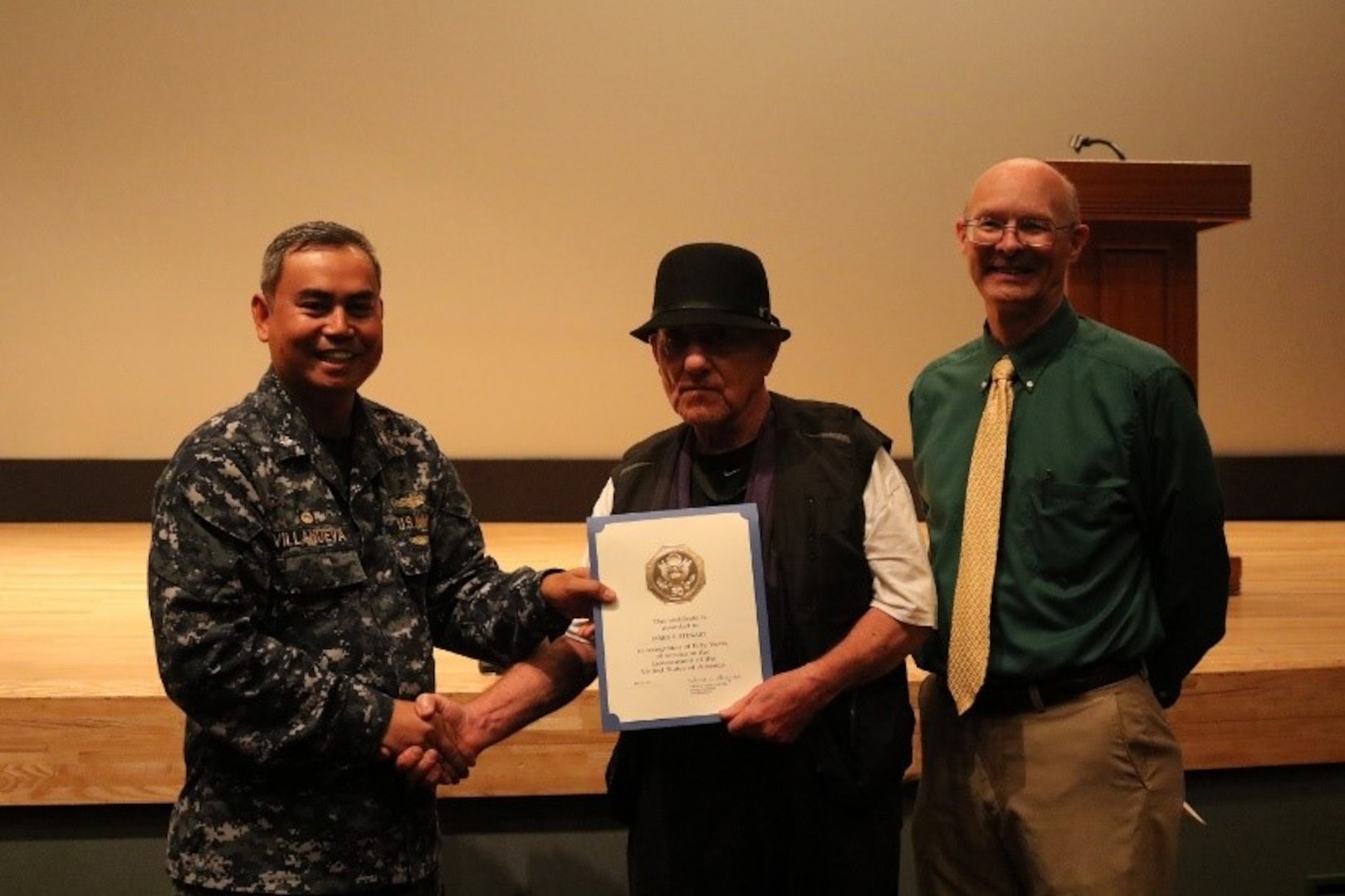 James Stewart, center, Receiving Branch materiel handler, is presented a 50-year Federal service certificate, pin and letter on behalf of the DLA Director by DLA Distribution Yokosuka, Japan, commanding officer Cmdr. Nolasco Villanueva, left, and deputy commander Roy Jewell.