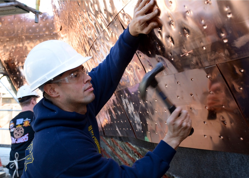 Navy Petty Officer 3rd Class Jorge Ortiz, assigned to the USS Constitution, hammers a copper nail into the new copper sheets that line the hull of the ship, which is dry docked in the Charlestown Navy Yard in Boston, Oct. 20, 2016. The USS Constitution was undergoing a multiyear restoration in Dry Dock 1, the second oldest dry dock in the United States. Navy photo by Petty Officer 3rd Class William Collins III