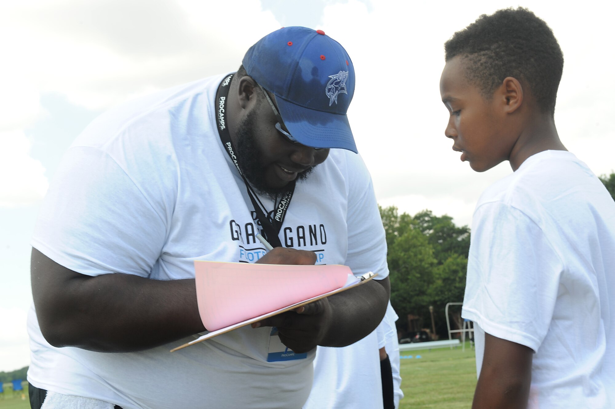(Left) Jonathan Brown, a volunteer football coach from Elizabeth City State University, N.C., signs in a participant during a youth football camp at Joint Base Langley-Eustis, Va., July 19, 2017. Football coaches from different schools throughout the area volunteered their time to help train and coach the military children during the camp. (U.S. Air Force photo/Staff Sgt. Brittany E. N. Murphy)