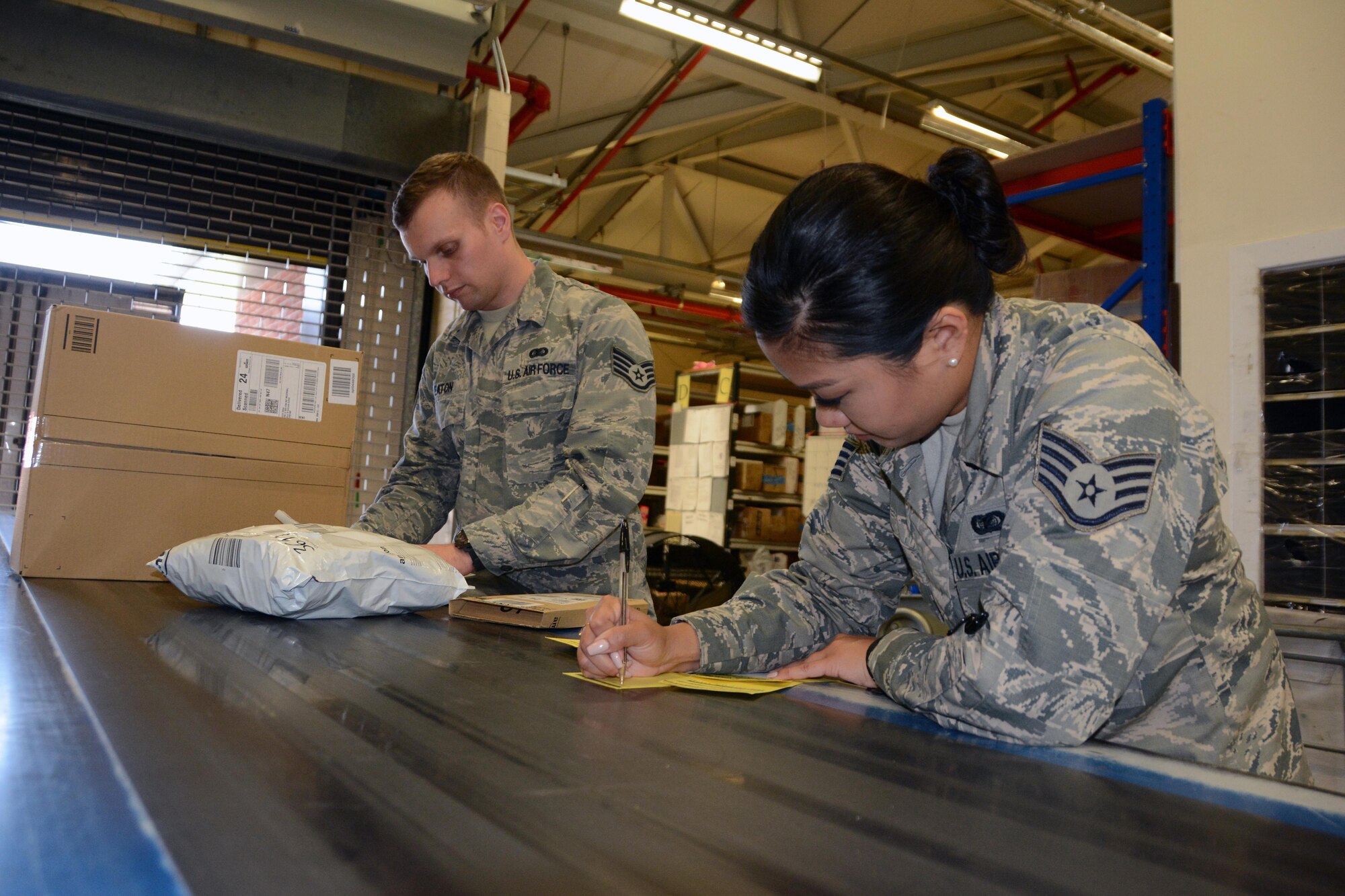 U.S. Air Force Staff Sgts. Douglas Eaton and Hyeyun Nam, 100th Communications Squadron Post Office postal clerks, work together to manually log in new parcels July 18, 2017, at RAF Mildenhall, England. The new system, scheduled to take effect Aug. 14, will allow email notifications to be sent to customers when their packages have arrived at the post office. (U.S. Air Force photo by Tech. Sgt. Lauren Gleason)