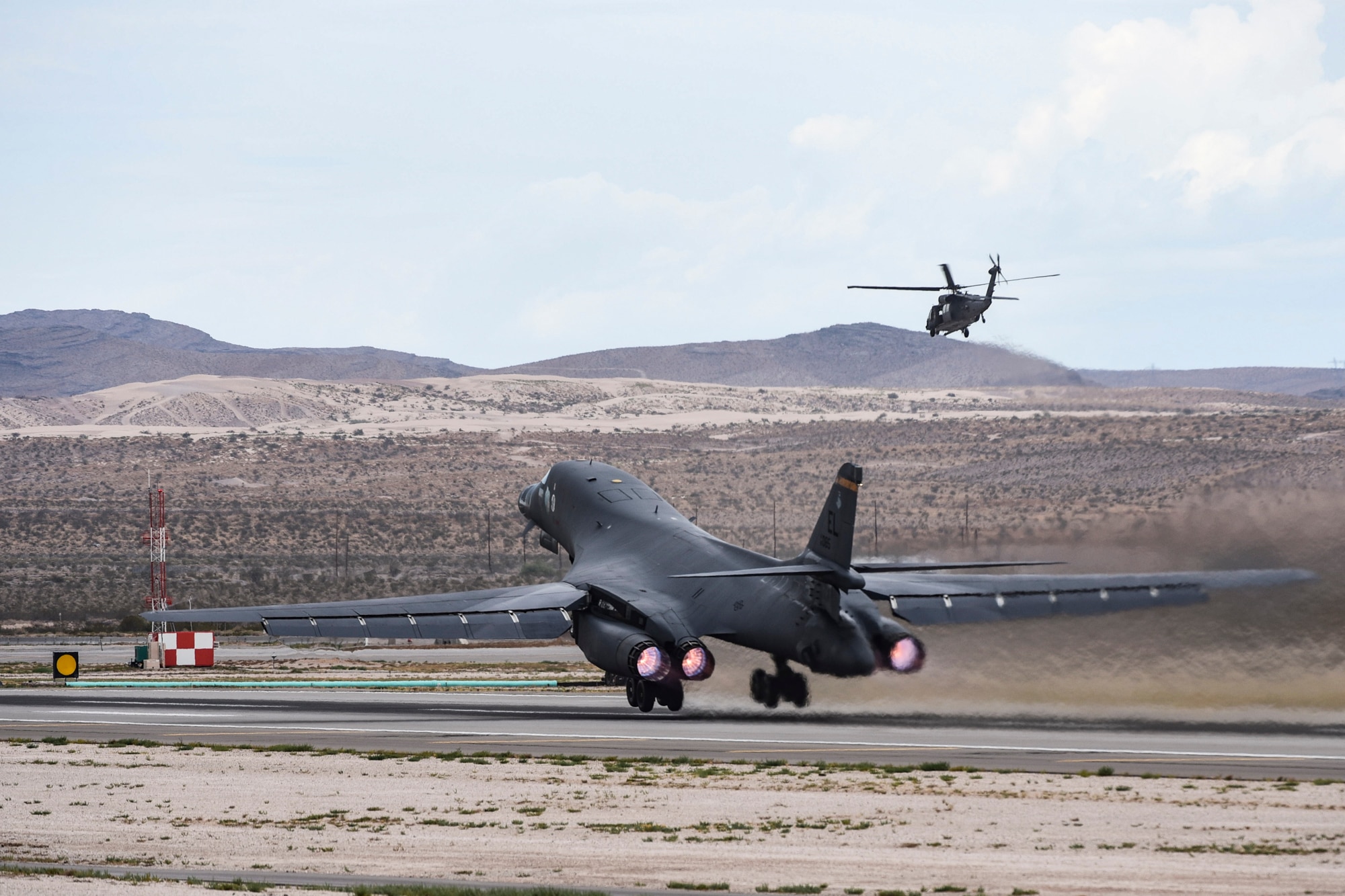 A B-1B Lancer from the 34th Bomber Squadron, Ellsworth Air Force Base, S.D., takes off as an HH-60G Pave Hawk helicopter from the 66th Rescue Squadron flies in the background during Red Flag 17-3 at Nellis Air Force Base, Nev. July 24, 2017. Red Flag 17-3 is primarily conducted over the Nevada Test and Training Range, 2.9 million acres of land and 5,000 square miles of airspace restricted from civilian air traffic over-flight. (U.S. Air Force photo by Airman 1st Class Andrew D. Sarver/Released)