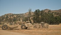 Engineers drive a grader and a scraper by each other while improving the roads and motor pool of the 718th Engineer Company's command post during training in Fort Hunter Liggett, Calif., on July 19, 2017. The engineers had to conduct operations while under threat of simulated attack by opposing forces. Nearly 5,400 service members from the U.S. Army Reserve Command, U.S. Army, Army National Guard, U.S. Navy, and Canadian Armed Forces are training at Fort Hunter Liggett as part of the 84th Training Command’s CSTX 91-17- 03 and ARMEDCOM’s Global Medic; this is a unique training opportunity that allows U.S. Army Reserve units to train alongside their multi-component and joint partners as part of the America’s Army Reserve evolution into the most lethal Federal Reserve force in the history of the nation. (U.S. Army Reserve photo by Sgt. David L. Nye, 301st Public Affairs Detachment)