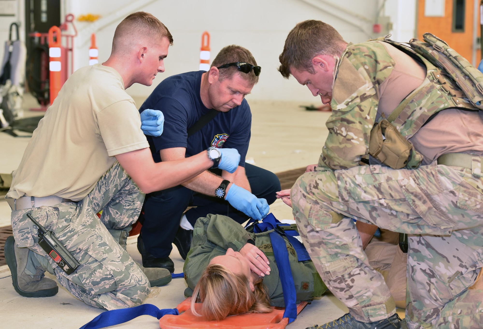 Airman 1st Class Brian Mclain, left, and Gene Carlander, middle, 45th Civil Engineer Squadron firefighters, secure active shooter exercise victim Senior Airman Kristina Kruger, 920th Force Support Squadron, onto a stretcher for transport to the hospital while 1st Lt. Ryan Kelly, right, 38th Rescue Squadron combat rescue officer, annotates her status update July 25, 2017 in Hangar 750. The firefighter and pararescue teams worked together closely to tend to victims on scene. The joint exercise between the 920th Rescue Wing and 45th Space Wing tested the units’ ability to work together in an emergency situation. (U.S. Air Force photo/Tech. Sgt. Lindsey Maurice)