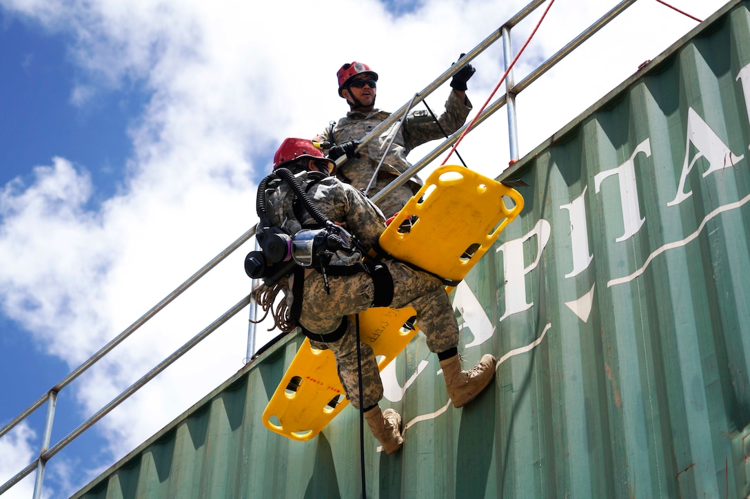 A Hawaii Army National Guardsman rappels with a medical backboard down the side of a structure during a combined training exercise in Kalaeloa, Hawaii, July 18, 2017. Air National Guard photo by Tech. Sgt. Andrew Jackson