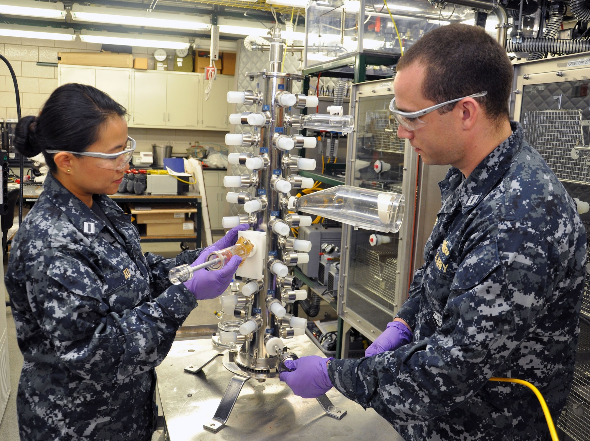 Lt.s Dan Xu (left), a Navy Research Biochemist, and Joshua Roaf (right), a naval surface warfare officer and graduate intern on site at the Naval Medical Research Unit - Dayton as part of his master's program in toxicology at The University of North Carolina at Chapel Hill, work to draw a filter sample for contaminant verification of particulate matter during a test at NAMRU-D's Environmental Health Effects Laboratory July 25 (U.S. Air Force photo/Bryan Ripple).