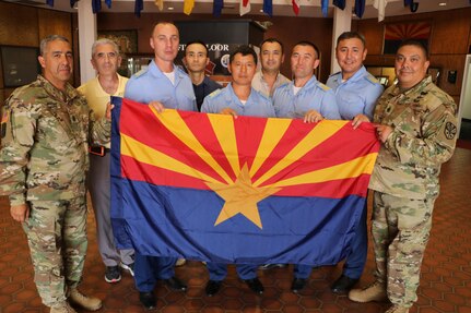 Command Sgt. Major Fidel Zamora, the senior enlisted advisor for the Arizona Army National Guard and Command Sgt. Major Saul Garcia, the command sergeant major for the 98th Aviation Troop Command, hold the Arizona state flag with delegates from Kazakhstan during a visit to exchange aviation maintenance practices and non-commissioned officer development July 25, 2017. The visit came within weeks of the U.S. government’s formal renewal of its partnership with Kazakhstan, extending the 24-year-old legacy of cooperation for five more years. 