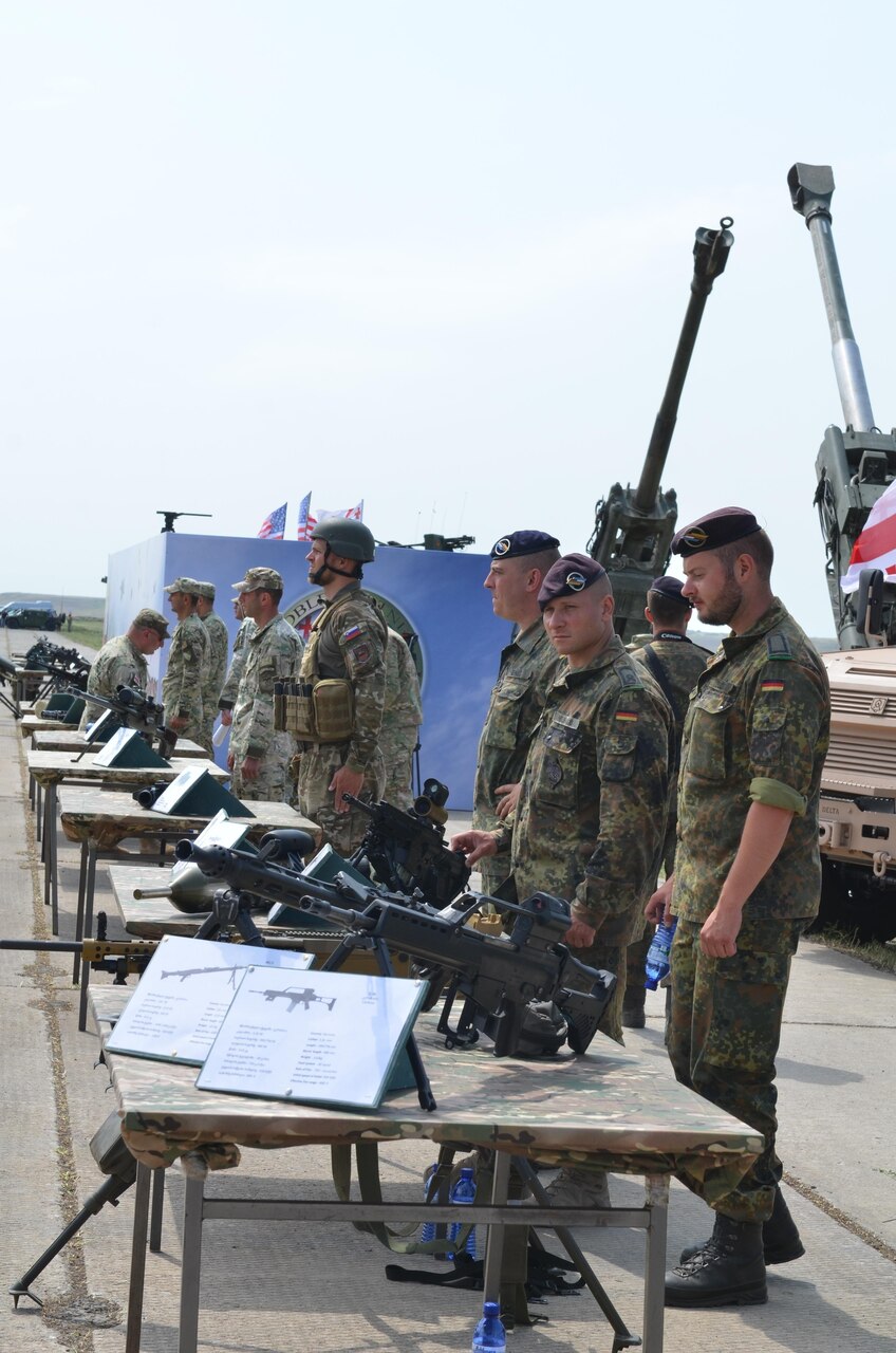 From right, German, Slovenian and Georgian troops man tables displaying their countries' weapons during the opening ceremonies for exercise Noble Partner at Vaziani Military Base, Georgia, July 30, 2017. Army photo by Sgt. Shiloh Capers