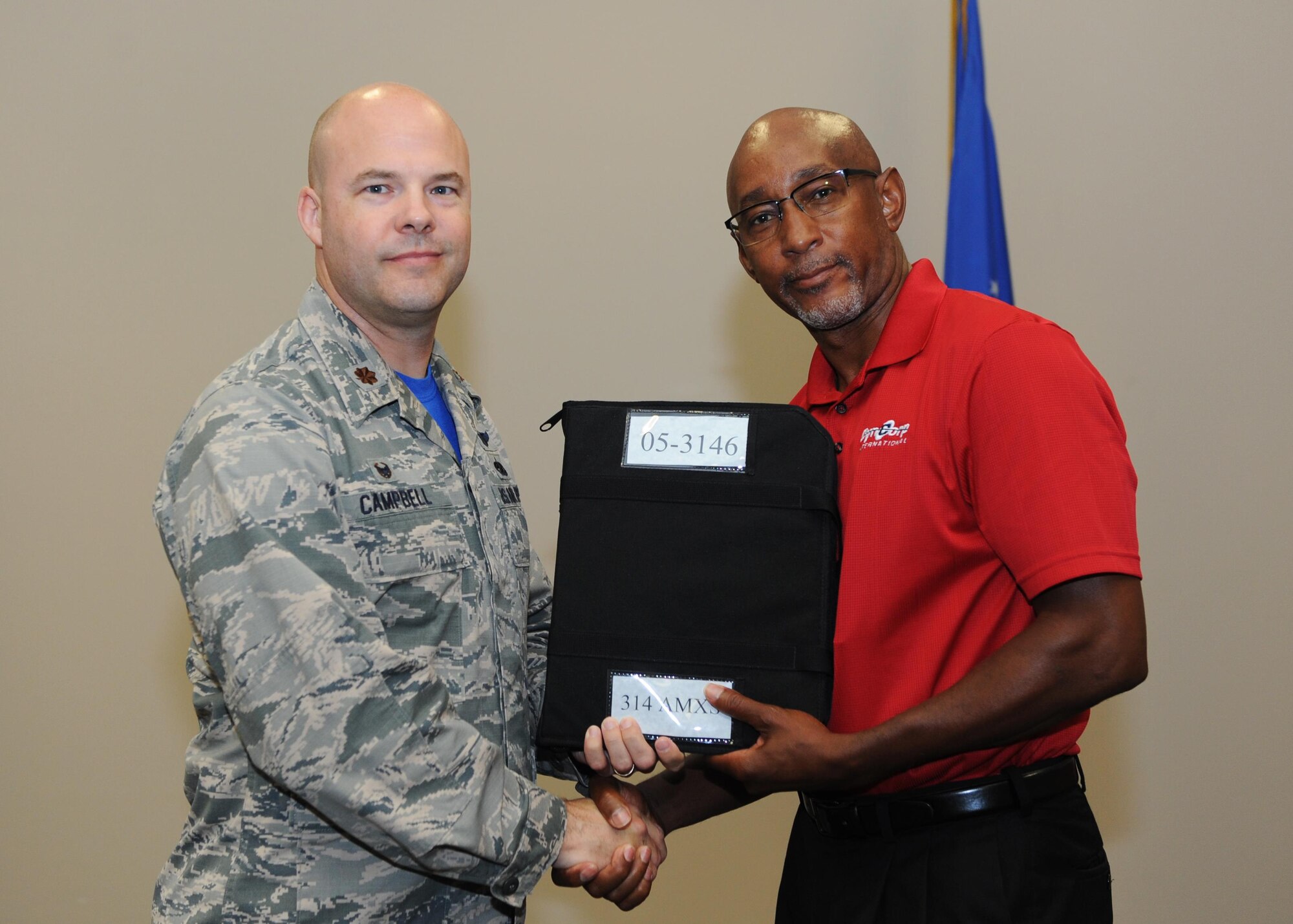 Maj. Paul Campbell, 314th Aircraft Maintenance Squadron commander, presents Joseph Lowe, DynCorp International contractor, a binder June 30, 2017, at Little Rock Air Force Base, Ark. The presentation of the binder signifies the end of a six-month transition between the 314th AMXS Airmen and DynCorp International employees. (U.S. Air Force photo by Airman 1st Class Grace Nichols)