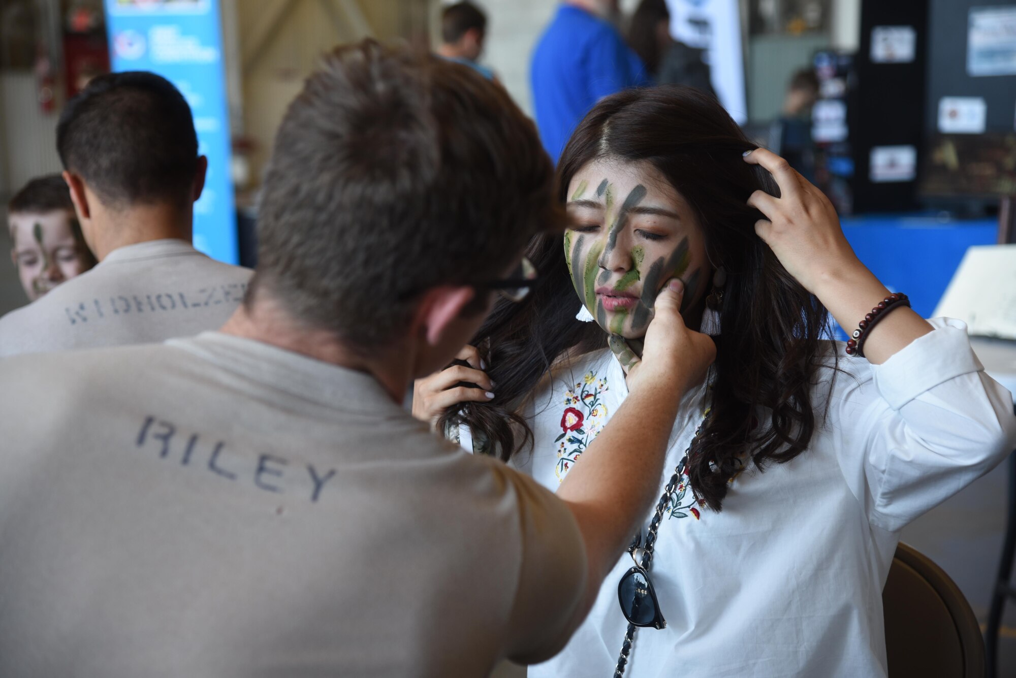 Senior Airman James Riley, Survival Evasion Resistance and Escape specialist, applies camouflage paint a visitors face during the SkyFest 2017 Air Show and Open House July 30, 2017, at Fairchild Air Force Base, Washington. SkyFest 2017 is a community event  to inform the public about Air Force assets and to showcase the capabilities of its aircraft. (U.S. Air Force photo/Senior Airman Nick J. Daniello)