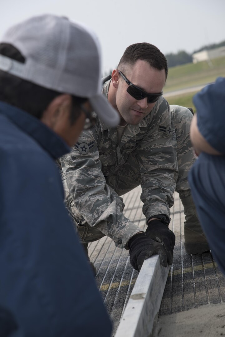 U.S. Air Force Airman 1st Class Samuel Hooper, a 35th Civil Engineer Squadron heavy equipment and pavement technician, works with Yoshinobu Ongasawara, a Japanese contractor, to level concrete on the flight line at Misawa Air Base, Japan, May 23, 2017. The 35th CES worked several weeks with contractors to reconstruct the airfield. (U.S. Air Force photo by Airman 1st Class Sadie Colbert)