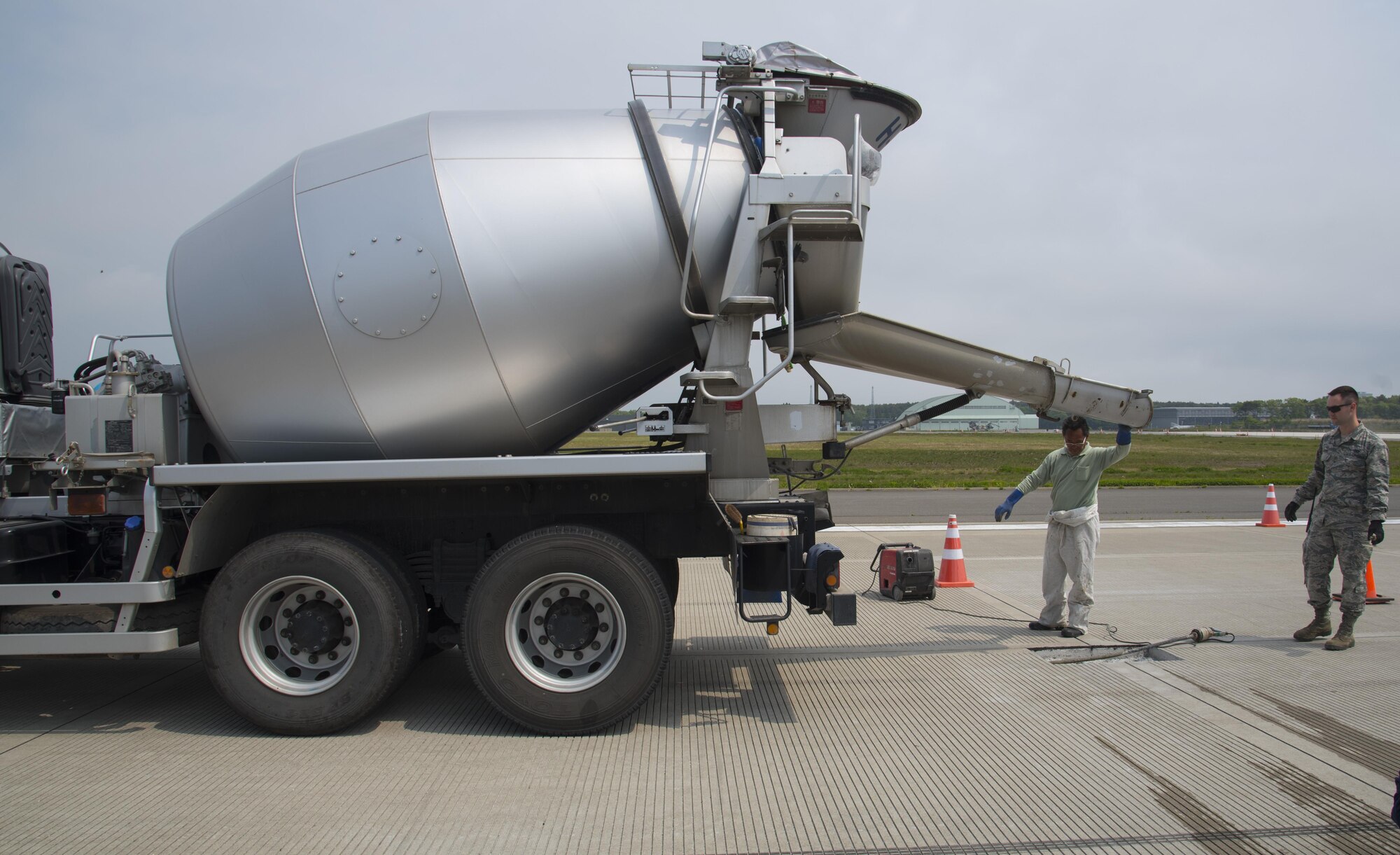 Hiroshi Nakasato, a Japanese contractor, left, readies a concrete truck to fill a spall on the flight line as U.S. Air Force Airman 1st Class Samuel Hooper, a 35th Civil Engineer Squadron heavy equipment and pavement technician, watches, at Misawa Air Base, Japan, May 23, 3017. Concrete is a a mixture of cement, various rocks, water and wood or magnesium. (U.S. Air Force photo by Airman 1st Class Sadie Colbert)