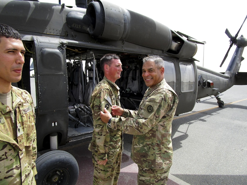 Lt. Gen. Michael Garrett, the commanding general of U.S. Army Central, presents Spc. Benjamin Baldwin, a UH-60 Blackhawk helicopter crew chief, for A Company, 2nd General Support Aviation Battalion, 149th Aviation Regiment, with his first combat patch, during an impromptu combat patch ceremony on the helicopter landing pad, on Ali Al Salem Air Base, May 20. Garrett surprised the crew chiefs with the impromptu stop and shared his story of how he received his first combat patch.  (U.S. Army photo by Lt. Col. Derek Johnson, USARCENT)