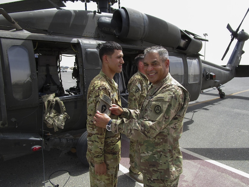 Lt. Gen. Michael Garrett, the commanding general of U.S. Army Central, presents Spc. Jesus Santiago, a UH-60 Blackhawk helicopter crew chief, for A Company, 2nd General Support Aviation Battalion, 149th Aviation Regiment, with his first combat patch, during an impromptu combat patch ceremony on the helicopter landing pad, on Ali Al Salem Air Base, May 20. Garrett surprised the crew chiefs with the impromptu stop and shared his story of how he received his first combat patch.  (U.S. Army photo by Lt. Col. Derek Johnson, USARCENT)